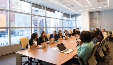 Coworkers smiling and discussing in the office, around a big wooden table